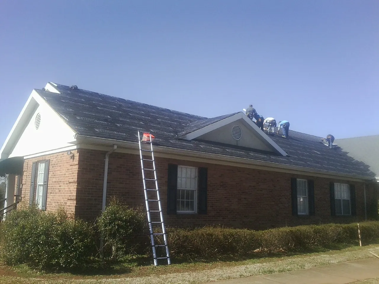 Crew tearing shingles off a brick ranch roof with a ladder set — Emergency Roof Repair work by our crew in Montague