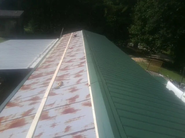 Old rusted panels beside newly installed green metal roofing — Wind Damage Roof Repair by Roofing Brothers in Montague